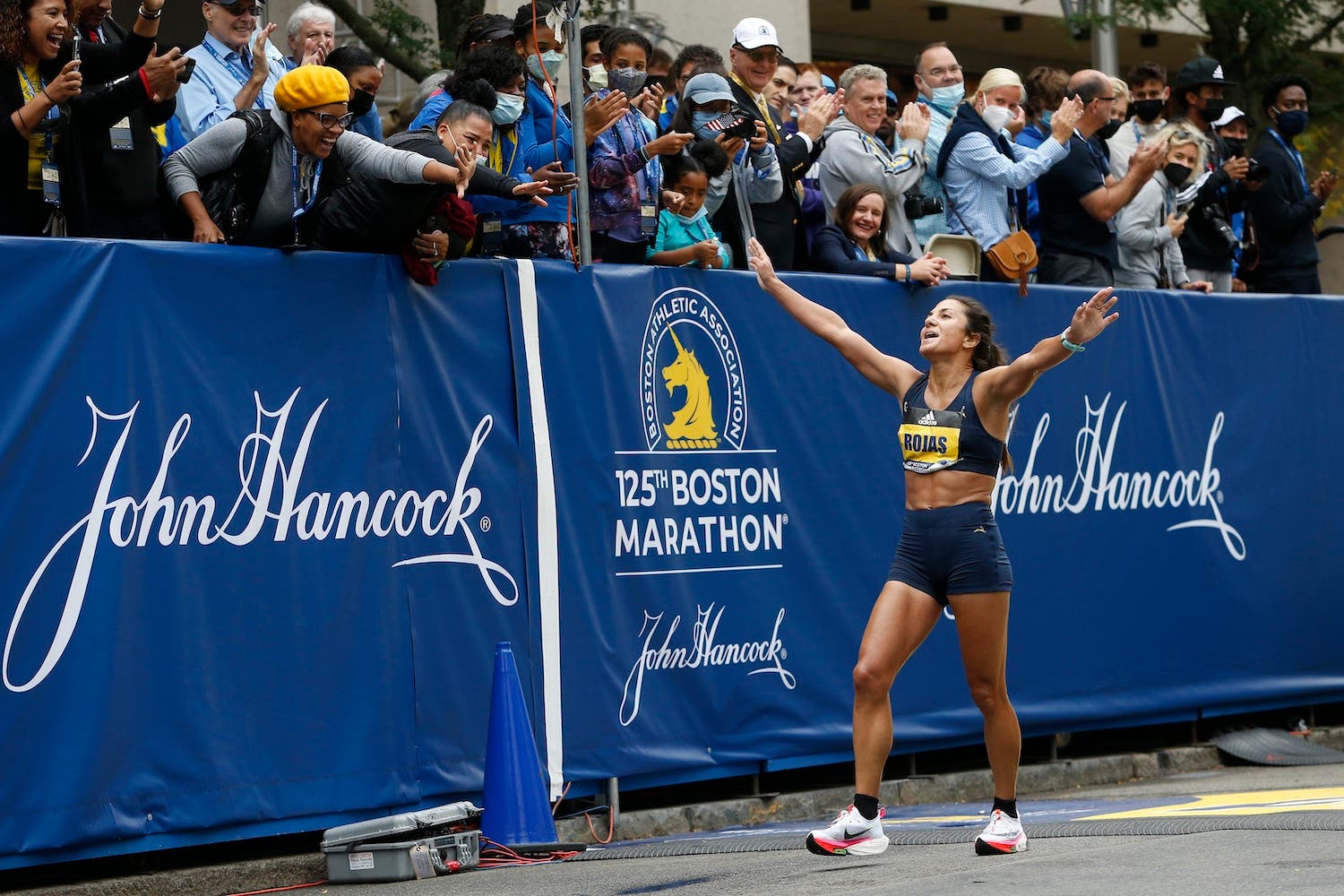 A top finisher at the Boston Marathon is cheered by fans in the stands behind her.